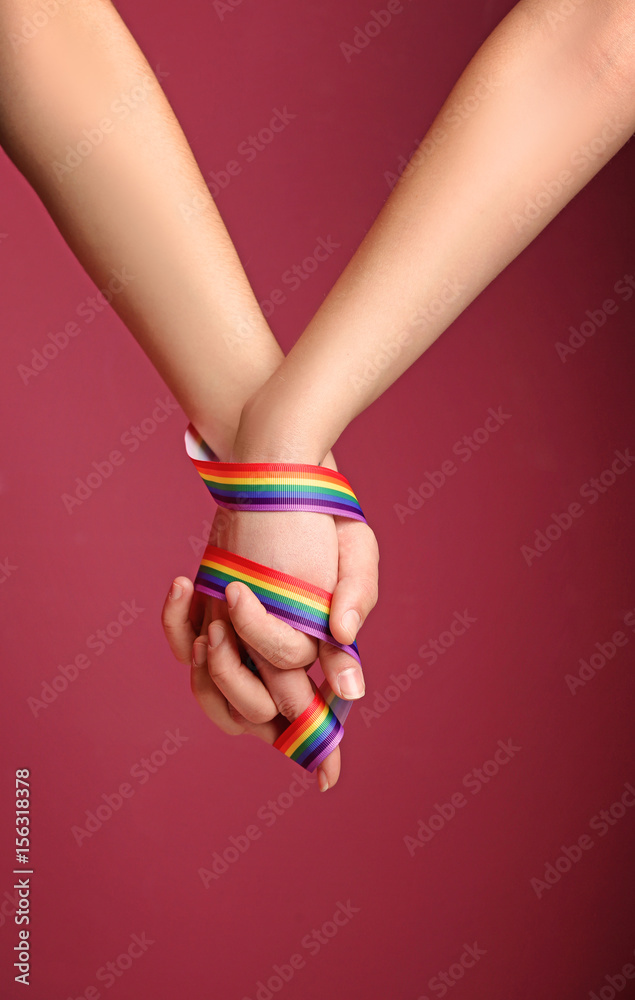 Young lesbian couple with rainbow ribbon on color background Young lesbian couple with rainbow ribbon on color background
