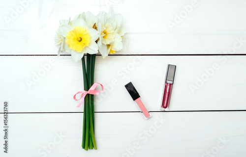 Top view on white wooden background with lip gloss and bouquet of narcissus. Liquid Lipstick