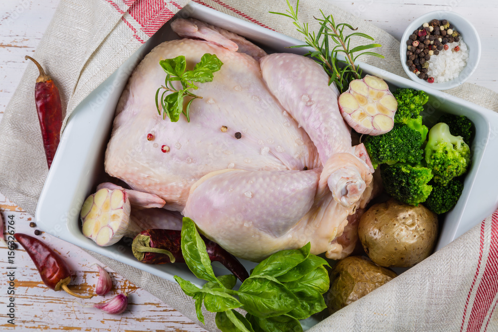 Raw whole chicken with herbs and spices on rustic wood background Raw whole chicken with herbs and spices on rustic wood background