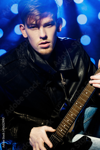 young attractive rock musician playing electric guitar and singing. Rock star on background of spotlights © producer