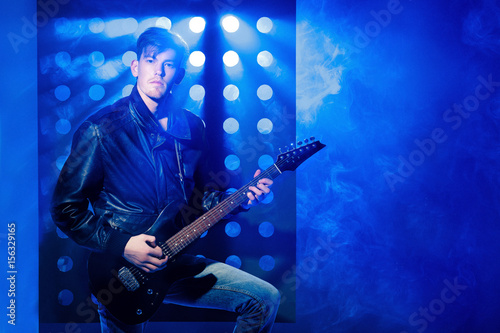young attractive rock musician playing electric guitar and singing. Rock star on background of spotlights