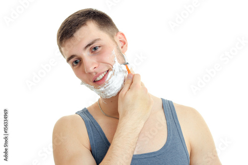a cheerful young man with foam on his face worth bending head smiling and shaves his beard is isolated on a white background