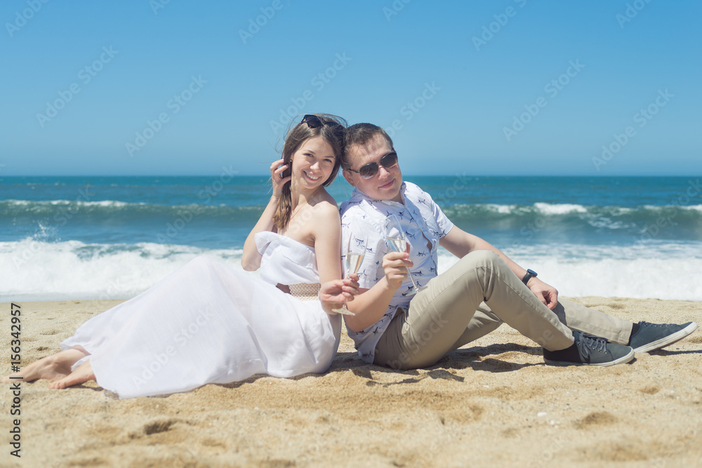 Young romantic couple sitting on the beach drinking champaign