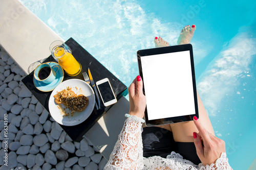Woman using digital tablet while sitting in swimming pool