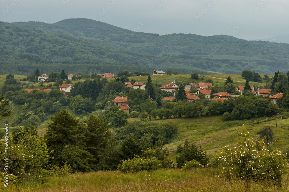 Scene with mountain glade, forest and residential district of bulgarian village Plana, Plana mountain, Bulgaria 