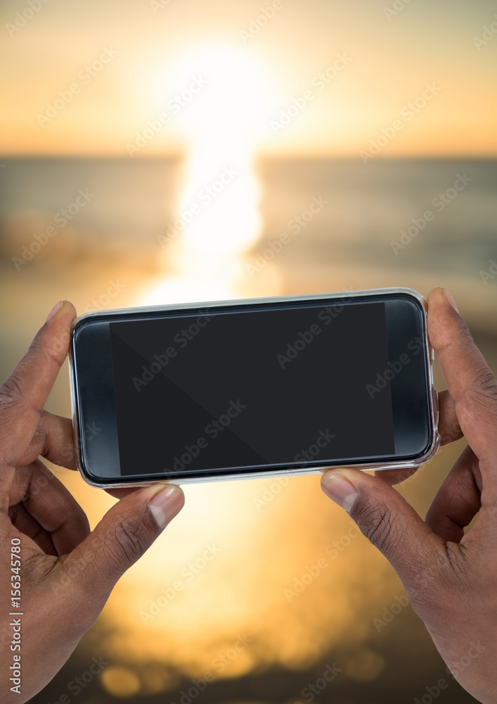 Hands with phone against blurry sunset beach