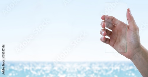 Hand with glass device against blurry water on sunny day
