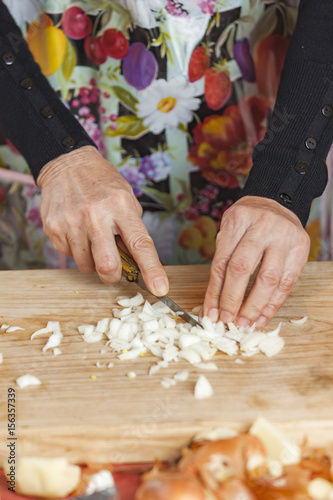 Senior old woman chopping and cutting onions into small pieces with her kitche knife