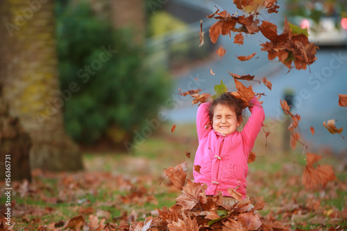 outdoor portrait of young happy child girl playing with autumn leaves in park on natural background
