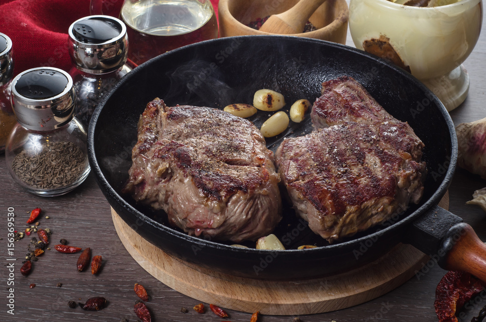 Grilled rib eye steak composition on grill iron pan on wooden background