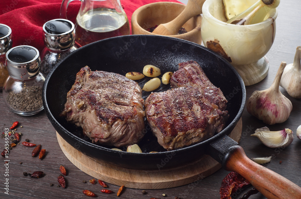 Grilled rib eye steak composition on grill iron pan on wooden background Grilled rib eye steak composition on grill iron pan on wooden background