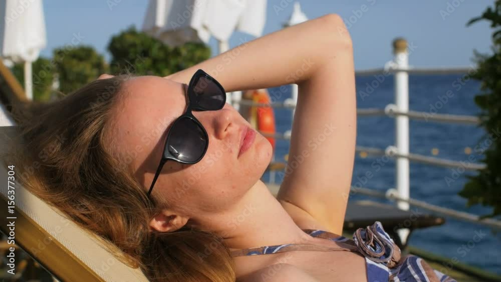 young relaxed blonde woman, lying on a lounger, touching hair, tanning and sunbathing, close-up young relaxed blonde woman, lying on a lounger, touching hair, tanning and sunbathing, close-up
