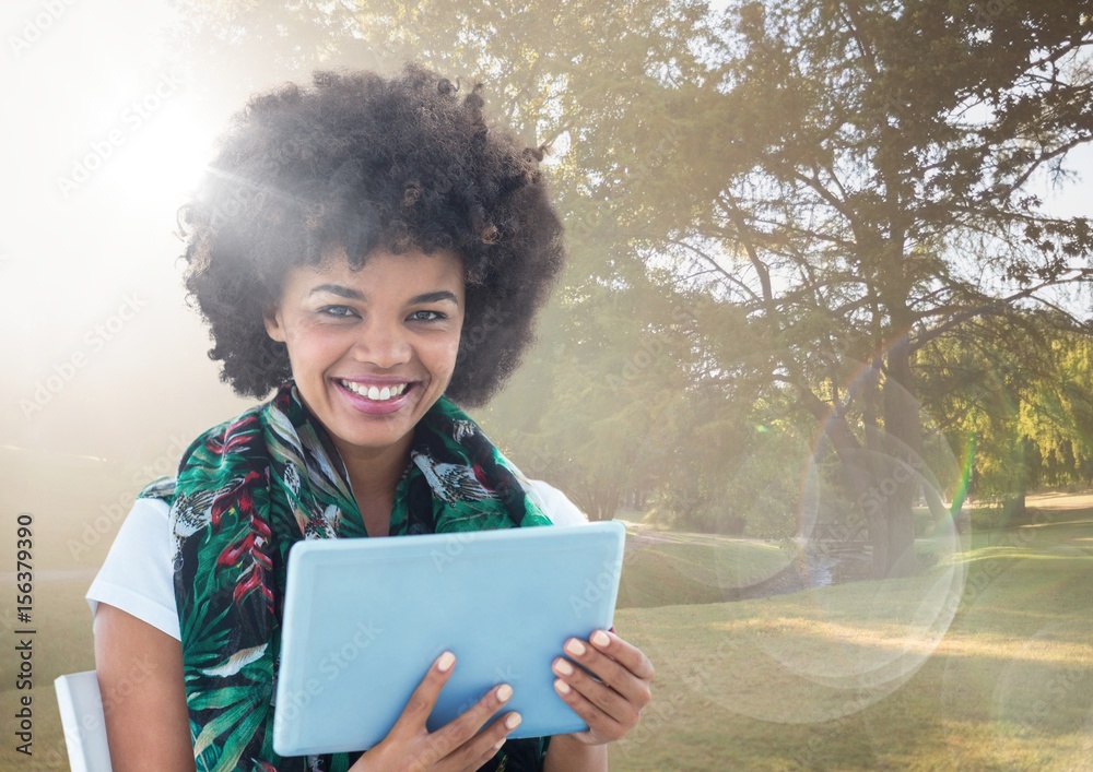 Woman with tablet against sunny park with flare Woman with tablet against sunny park with flare