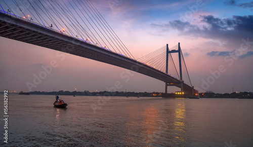Vidyasagar Seu (bridge) at twilight with a wooden boat on the river. The cable bridge connects Kolkata with Howrah district.
