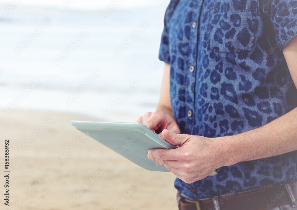 Trendy man mid section with tablet against blurry beach