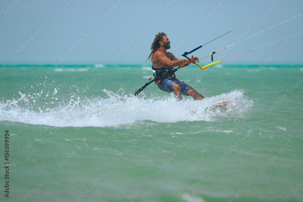 Kite surfer rides waves of the blue lagoon with kite flying in sky. Recreation activity and active extreme water sports kiteboarding, hobby and fun in vacation time, blue sea water, Egypt, Red Sea