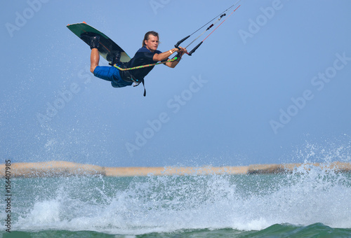 Professional kitesurfing rider sportsman jumps high acrobatics kiteboarding backroll trick  with huge water splash. Recreational activity and extreme active water sports, hobby and fun in summer time