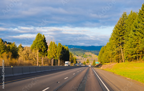 Amazing wide interstate highway in sunshine toll trees green divided concrete fens semi truck passenger cars cloudy sky