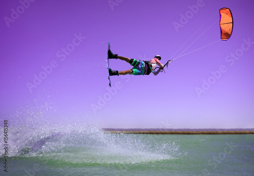 Professional kite boarding rider sportsman jumps high acrobatics kiteboarding raley trick  with huge water splash. Recreational activity and extreme active water sports, hobby and fun in summer time