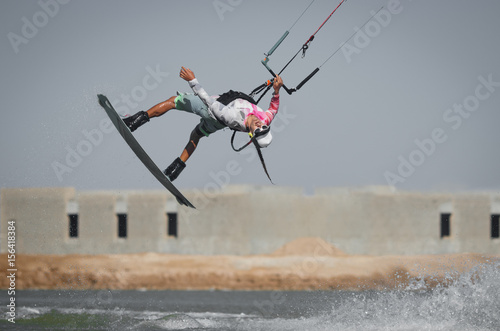 Professional kite boarding rider sportsman jumps high acrobatics kiteboarding tantrum trick with front rotation and water splash. Recreational activity and extreme active water sports, hobby and fun