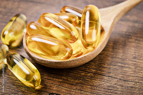 Fish oil capsules with omega 3 and vitamin D in a wooden spoon.