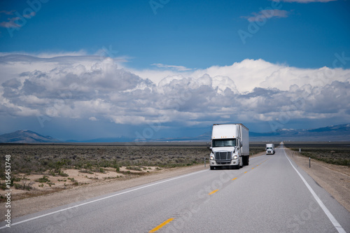 Semi trucks convoy on straight road in Nevada prairie