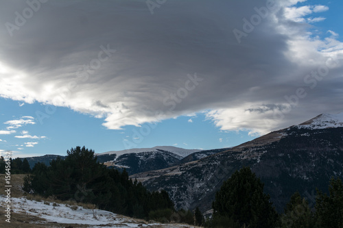 Large cloud above icy mountain peak in winter Pyrenees, Spain