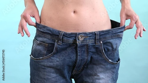 Thin girl show weight loss and old big jeans. Woman losing weight after diet, slim, burning fat and flat waist. Skinny female belly wearing too large pants. Getting in shape and reaching the goal