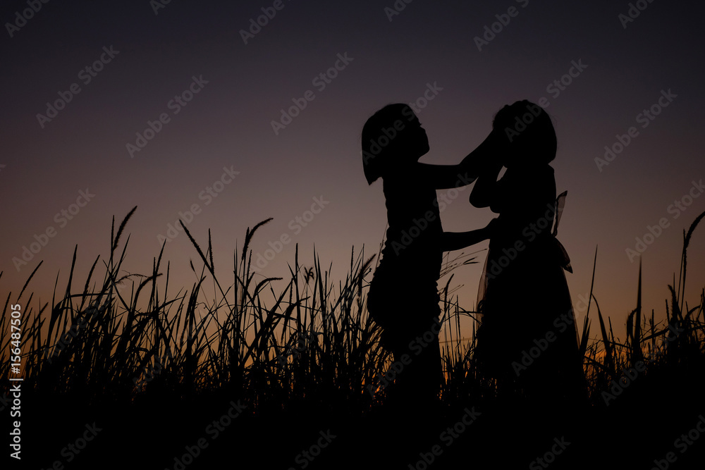 silhouette of a beautiful little girl standing on a grass field background of gorgeous sunsets. The girl giving promise and take care of each other. 