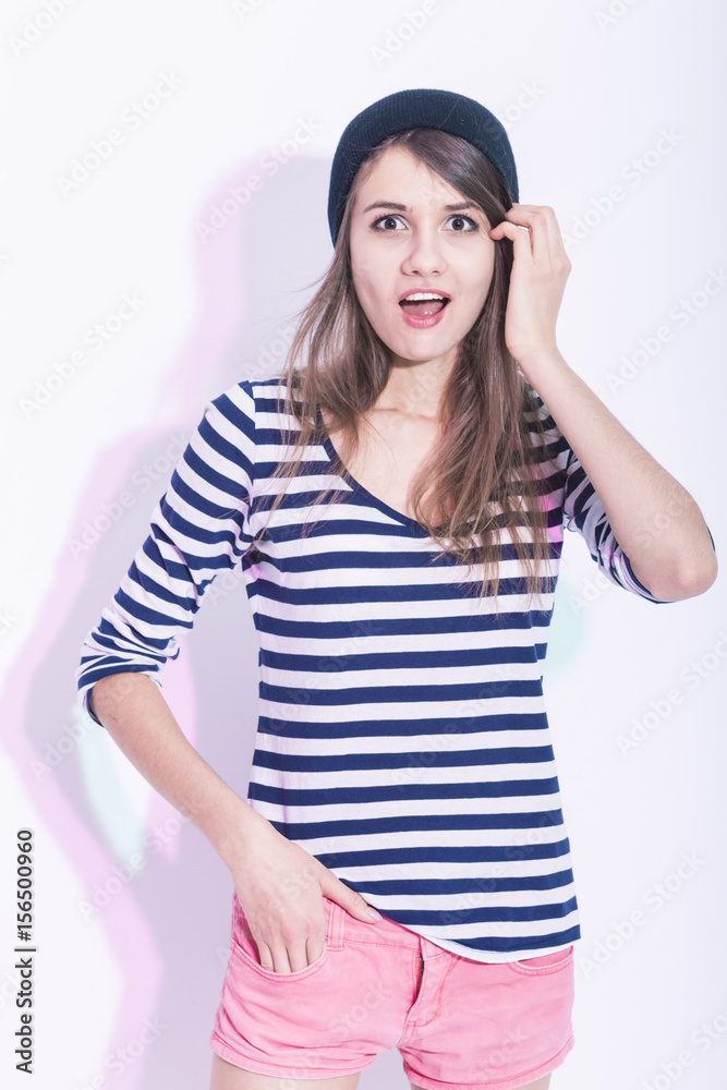 Portrait of Surprised Caucasian Brunette Girl in Hat and Striped Shirt. Posing Against White Background. Portrait of Surprised Caucasian Brunette Girl in Hat and Striped Shirt. Posing Against White Background.