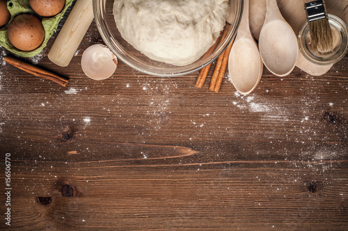 Cooking yeast dough for buns, butter, eggs, cooking equipment, flour on a wooden table. Top view with copy space, mockup for menu, recipe or culinary classes. Baking background.