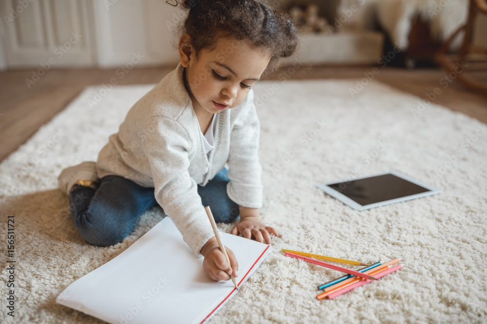 adorable little african american girl drawing with pencils and lying on carpet at home adorable little african american girl drawing with pencils and lying on carpet at home