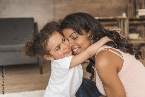 little daughter hugging smiling mother while spending time at home