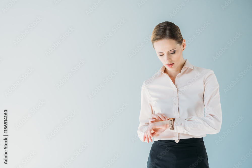 young attractive caucasian businesswoman in formalwear looking at hand watches, isolated on grey young attractive caucasian businesswoman in formalwear looking at hand watches, isolated on grey