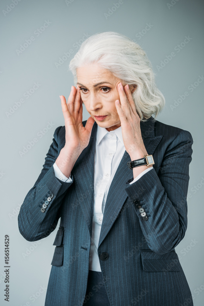 senior businesswoman in suit having headache isolated on grey senior businesswoman in suit having headache isolated on grey