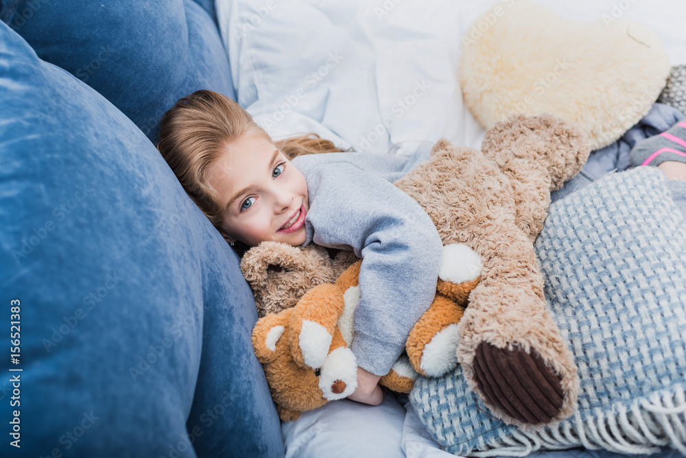 Adorable little girl lying on bed with teddy bears and smiling at camera Adorable little girl lying on bed with teddy bears and smiling at camera