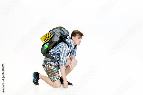 Young tourist with backpack ties up shoelaces on white background
