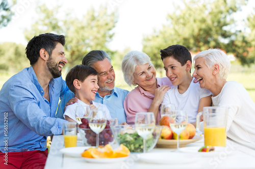 Family sitting at table outdoors, smiling 