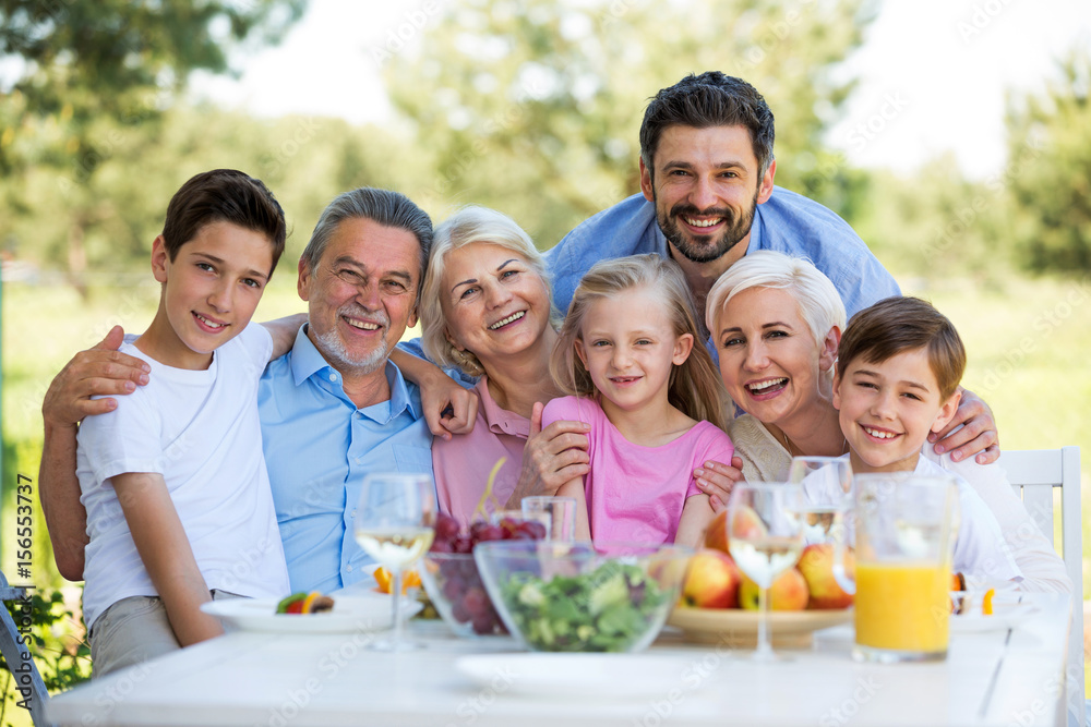 Family sitting at table outdoors, smiling
