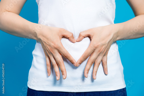 young woman who makes a heart shape by hands on her stomach. photo