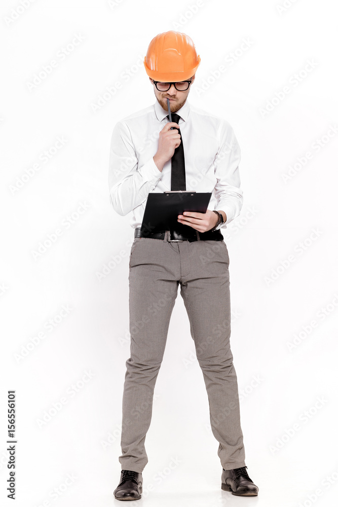 Young construction engineer in orange helmet with folder thinking on white background Young construction engineer in orange helmet with folder thinking on white background