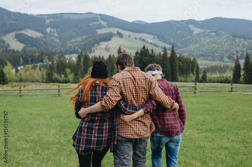 Three friends hugging and walking away. Boy and two girls traveling in mountains. 