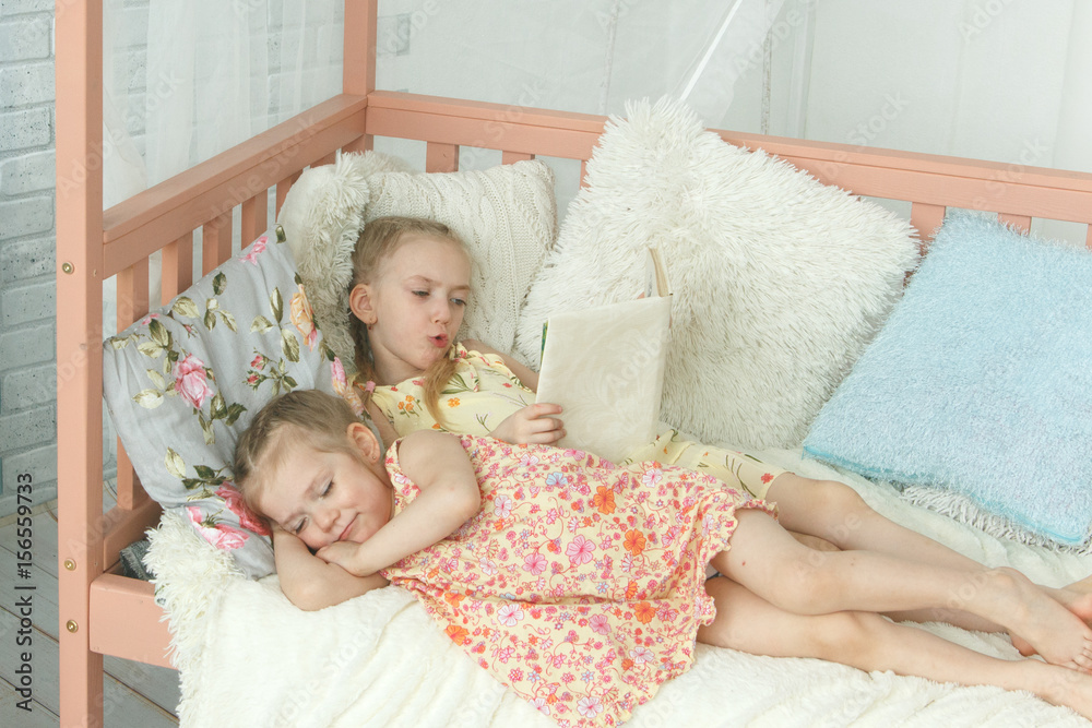 Older sister reading a book to her younger sister Older sister reading a book to her younger sister