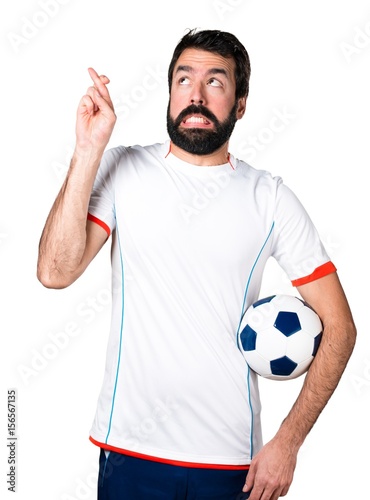 Football player holding a soccer ball with his fingers crossing
