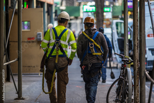Two construction workers walk together down a New York City sidewalk