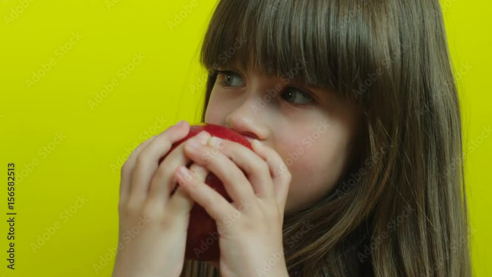 Handsome little girl trying to eat big delicious red apple. Kid eating apple. Yellow background. Close up. Slow motion Handsome little girl trying to eat big delicious red apple. Kid eating apple. Yellow background. Close up. Slow motion