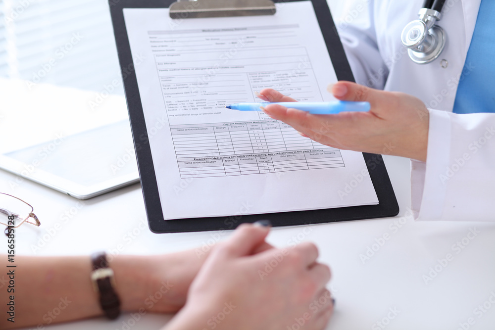 Close up of a doctor and patient hands while phisician pointing into medical history form at clipboard Close up of a doctor and patient hands while phisician pointing into medical history form at clipboard