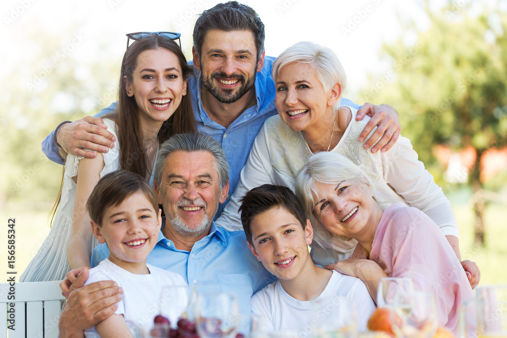 Family sitting at table outdoors, smiling
