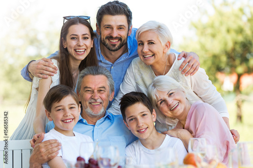 Family sitting at table outdoors, smiling
