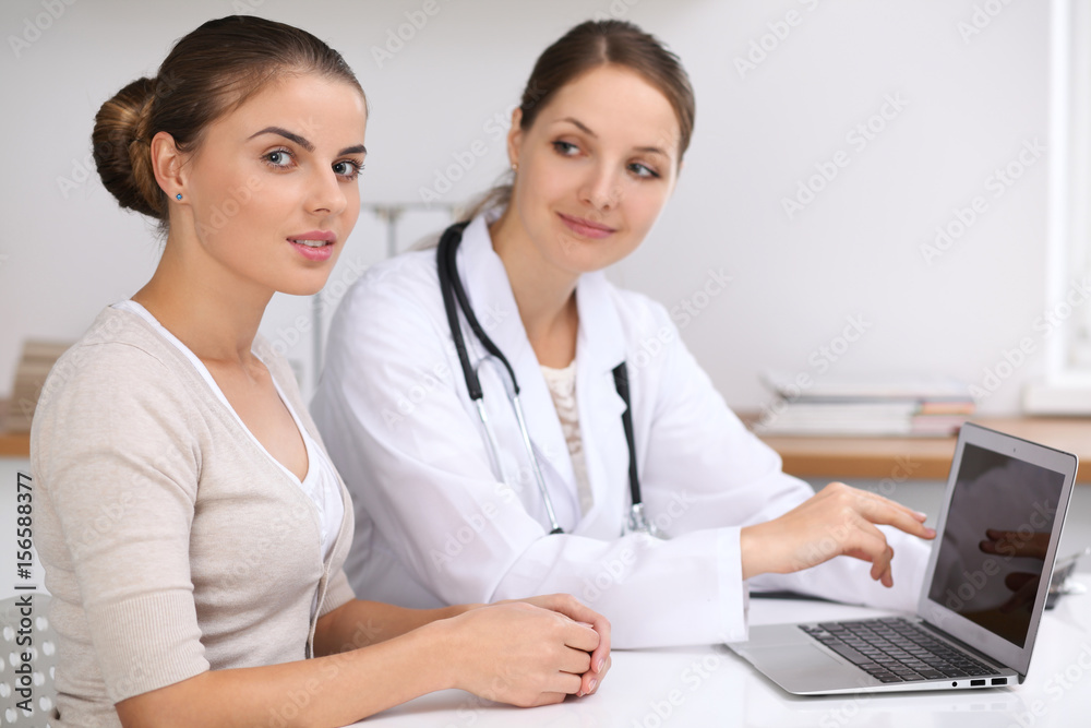 Doctor and patient sitting at the desk. Physician pointing into laptop computer. Medicine and health care concept Doctor and patient sitting at the desk. Physician pointing into laptop computer. Medicine and health care concept